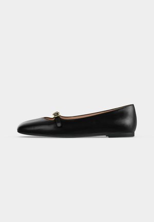 Black leather flat shoe with rounded toe and a small gold buckle strap across the top, against a plain light background.