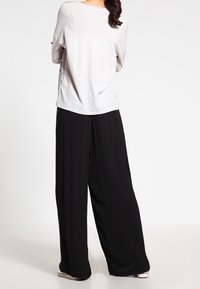 Maglietta grigia chiaro dalla vestibilità ampia con spalle scese abbinata a pantaloni neri larghi. Tessuto morbido con texture minimale e un sottile dettaglio a motivo laterale.