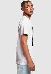 Hvid bomulds t-shirt med korte ærmer, der har et grafisk tryk i sort. Pasformen er afslappet, og teksturen ser blød ud.