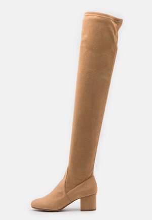 Bottes hautes en daim beige clair dépassant le genou, avec talon carré et bout arrondi.