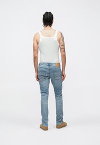 Λευκό φανελάκι και ανοιχτόχρωμα τζιν με ευθεία εφαρμογή, πίσω τσέπες και δερμάτινο ταμπελάκι στη μέση. Η εμφάνιση ολοκληρώνεται με παπούτσια σε ταμπά χρώμα.