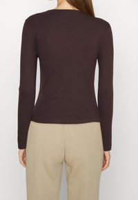 Brązowa bluzka z długim rękawem o prążkowanej fakturze i okrągłym dekolcie, w połączeniu z beżowymi spodniami. Odzież dobrze przylega do ciała i ma prosty dół.