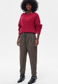 Czerwony sweter z dzianiny z teksturowanym wzorem, w połączeniu z luźnymi brązowymi spodniami ze sznurkiem. Czarne botki za kostkę z ozdobnymi klamrami.