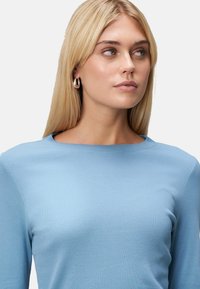 T-shirt à manches longues bleu clair avec un col rond, fabriqué dans un tissu doux. Présente une texture lisse et un design minimaliste.