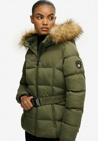 Chaqueta acolchada de color verde oliva con borde de capucha de pelaje sintético, cierre con cremallera, cinturilla con hebilla y parche con logo en la manga izquierda. Tejido acolchado texturizado.