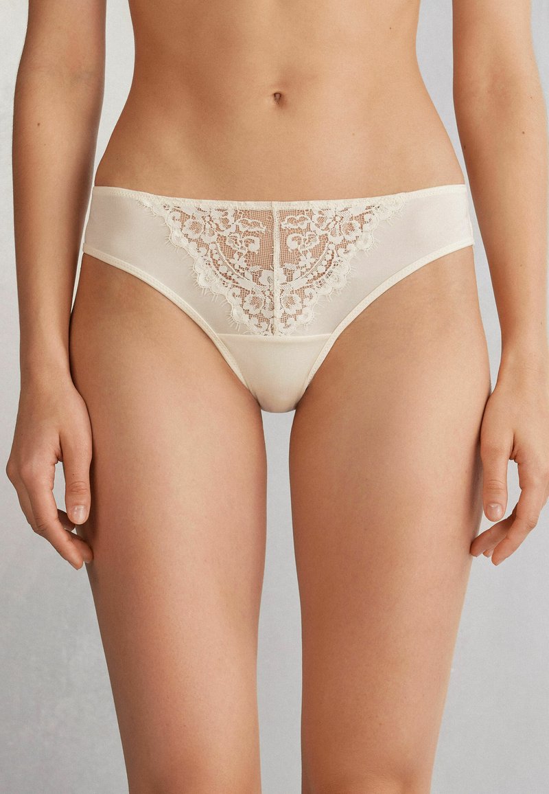Ivory lace panties with sheer texture, floral pattern, and scalloped detailing on the edges. Soft fabric construction for comfort.