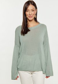Pulover tricotat de culoare verde deschis, cu o croială lejeră, umeri lăsați și o decolteu larg. Are o textură moale și manșete cu dantele.