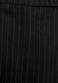 Schwarzer Stoff mit vertikalen weißen Streifen, leicht strukturiert, mit einer Nahaufnahme des gewebten Materials und einem Taschendetail.