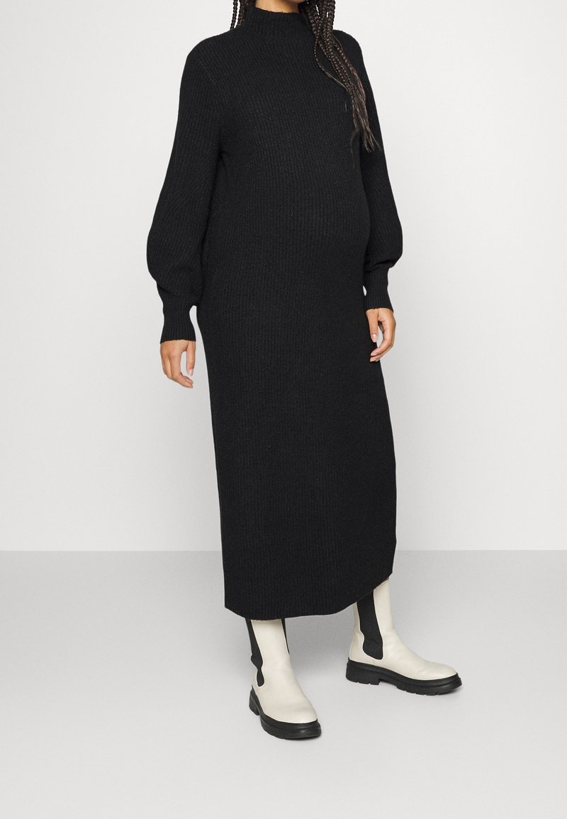 Musta neulottu maksimekko, jossa pitkät, pulleat hihat ja korkea kaulus. Päällä valkoiset nilkkurit, joissa mustat sivupaneelit ja paksu pohja.