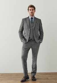 Grauer Anzug mit drei Teilen und strukturiertem Finish, weißes und blau gestreiftes Hemd, grün-weiß gestreifte Krawatte und braune formelle Schuhe.