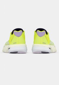 Zapatillas deportivas de un amarillo brillante con parte superior de malla texturizada, detalles morados en el talón, una entresuela blanca acolchada y suela de goma negra.