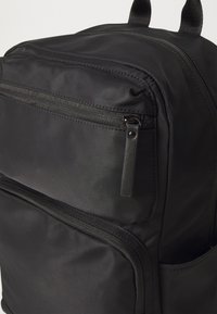 Černý látkový batoh s hladkou texturou, dvojitými zipovými oddíly a malou přední kapsou se černým zipem.