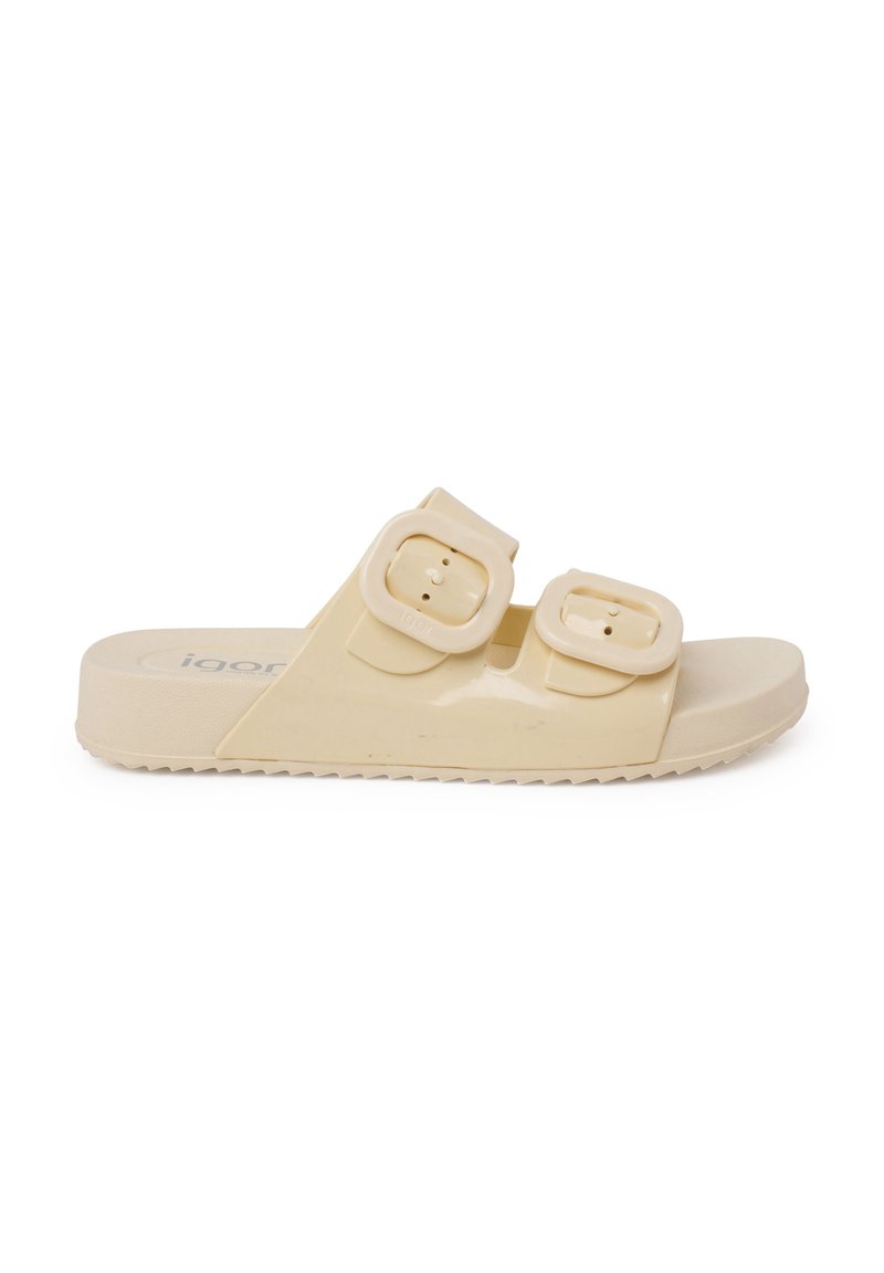 Light beige slide sandal made of glossy material featuring two adjustable buckles and a textured sole. Rounded toe with a flat design.