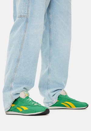 Zielono-żółte buty sportowe z gumową podeszwą, z sznurowanym wiązaniem i wyściełanym językiem, zestawione z jasnoniebieskimi, luźnymi dżinsami.