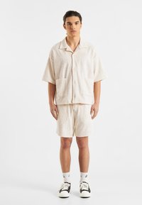 Lichtbeige kortarm overhemd en bijpassende shorts, getextureerd met een spiraalpatroon, met een kraag en voorzakken.