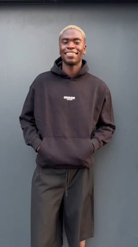 Felpa nera con cappuccio e tasca frontale, con logo bianco, abbinata a pantaloni corti neri. Design complessivo casual con una vestibilità rilassata.