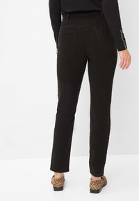 Pantaloni neri a gamba dritta con una texture liscia, dotati di due tasche posteriori e un elastico in vita. Abbinati a scarpe marroni con stampa leopardata.