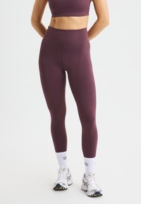 Bordeaux leggings met een hoge taille, gemaakt van rekbare stof. Voorzien van een gladde textuur en een aansluitend ontwerp, gecombineerd met witte sportkousen en schoenen.