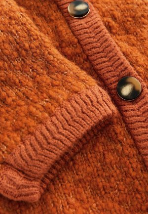 Rustfarvet strikket cardigan med en tekstureret krop, ribbede manchetter og krave samt to store sorte knapper foran.