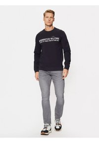 Felpa nera con testo bianco, jeans grigi e sneakers bianco e nere. Progettata per il comfort con una vestibilità rilassata.