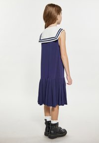 Kleider in Marineblau mit einem weißen Matrosenkragen, der marineblauen Streifen hat, einem gefältelten Rock und in Kombination mit schwarzen Stiefeln und weißen Spitzensocken getragen.