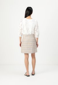 Bela cvetna čipkasta bluza s napihnjenimi rokavi, v kombinaciji s bež karirasto krilo. Outfit dopolnjujejo svetlo obarvane sandale s trakovi.