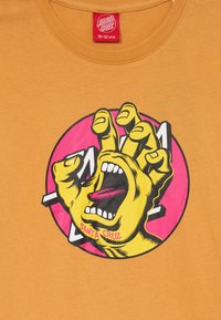 Gul grafisk T-shirt med en djärv, skrikande handdesign mot en rosa cirkel, med texten "Santa Cruz" i botten.