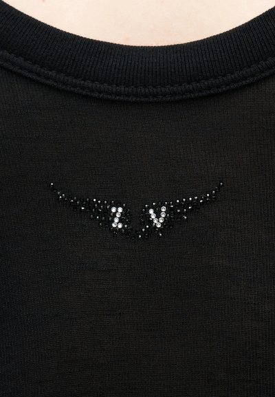 Μαύρο πλεκτό ύφασμα με μικρό σχέδιο λαμπερών μαύρων και λευκών χαντρών που σχηματίζουν τα γράμματα "ZV" με σχήματα που μοιάζουν με φτερά.