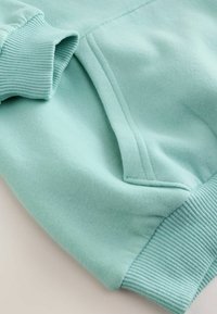 Piparmētru zaļš džemperis ar ribotām aprocēm, mīksta auduma tekstūra, kangoru kabata un gluda virsma. Izstrādāts komfortam un ikdienas valkāšanai.