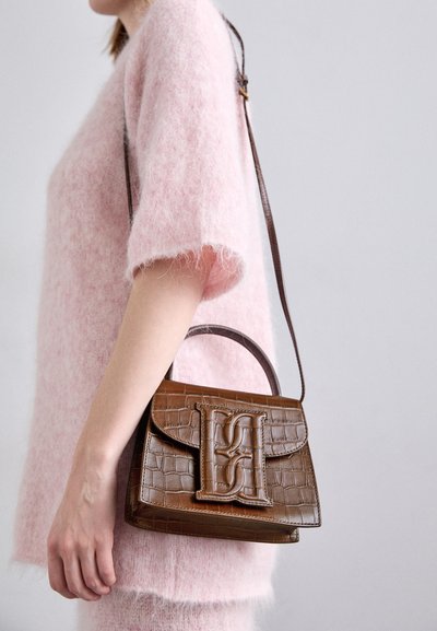Braune Handtasche aus Krokodilleder-Prägung mit einem oberen Griff und einem Schulterriemen. Besitzt ein auffälliges Logo auf der Frontklappe. Weiche Textur.