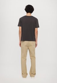 Donkergrijs crewneck T-shirt van katoen, gecombineerd met kaki wijde broek en witte sneakers. Achteraanzicht toont een relaxte pasvorm en eenvoudig ontwerp.