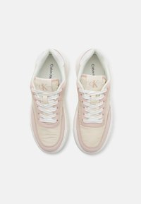 Adidașii Calvin Klein au un brâu de culoare bej și roz deschis, cu accente din suede, șireturi albe și o talpă din cauciuc, având o formă rotunjită.