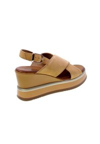 Sandalo a zeppa in suède color tan con punta aperta e cinturino sul retro, caratterizzato da una fascia decorativa argentata e una suola piatta in brown texturizzato.