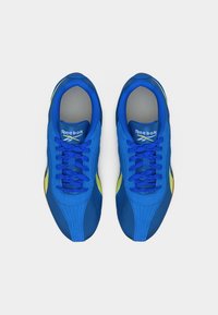 Ζευγάρι μπλε αθλητικά παπούτσια Reebok με κίτρινες λεπτομέρειες, σε λευκό φόντο, φωτογραφημένα από πάνω.