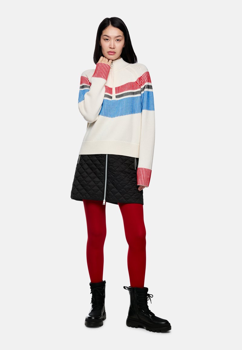 Knitted cream sweater with blue, red, and black horizontal stripes, paired with a black quilted skirt, red tights, and black lace-up boots.