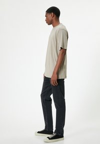 Camiseta de algodón beige con un corte relajado, combinada con jeans gris oscuro y zapatillas de lona negras con suelas de goma blanca.