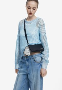 Light blue knitted sweater with open mesh texture, paired with light blue wide-leg jeans. Black crossbody bag with silver chain and snake print accent.