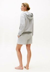 Felpa grigia in cotone con cappuccio e coulisse, abbinata a pantaloni corti grigi coordinati. L'outfit ha una vestibilità comoda e tasche laterali.