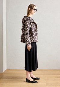 Jachetă cu imprimeu de leopard și glugă, fustă lungă neagră și balerini negri cu accesorii decorative. Textură netedă, croială ajustată, design modern.