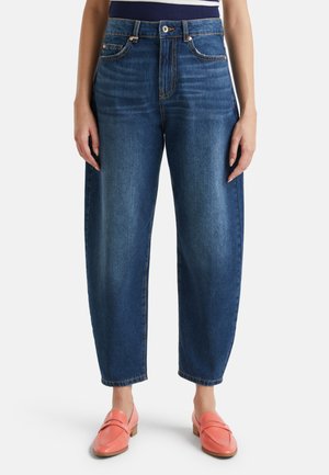 Jean taille haute bleu foncé avec une coupe décontractée, présentant cinq poches et un délavage subtil. Associé à des mocassins corail.