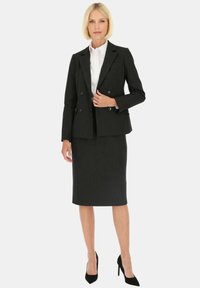 Dopasowana czarna marynarka z podwójnymi guzikami i teksturowanym materiałem, w połączeniu z dopasowaną czarną spódnicą i czarnymi szpilkami.
