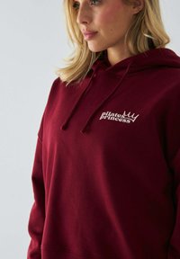 Bordowa bluza z kapturem z białym logo "Pilates Princess", o luźnym kroju, z regulowanym kapturem i miękkim, teksturowanym materiałem.