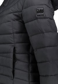 Schwarze Daunenjacke mit horizontalem Steppmuster, genähten Details und Logo-Patch auf der Schulter. Mit Reißverschlusstasche an der Seite.