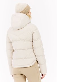 Leichte beige Daunenjacke mit Kapuze, gestepptem Design und elastischen Bündchen. Ergänzt durch eine beige und weiße Strickmütze.