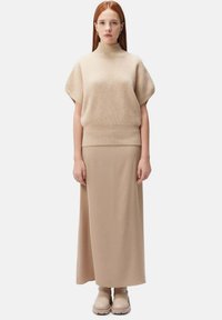 Ljusbeige räfflad stickad kortärmad polotröja och långkjol, båda i en slät, neutral nyans; robusta ljusbeiga ankelstövlar fulländar outfiten.