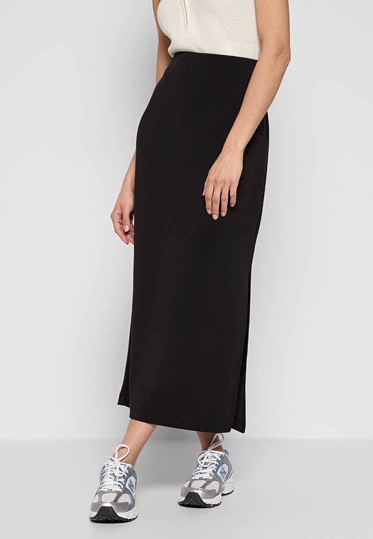 Gonna maxi nera con silhouette dritta, realizzata in un tessuto liscio. Abbinata a sneaker grigie e a un top senza maniche bianco.