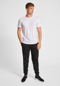 Hvid bomulds-t-shirt parret med sorte joggerbukser. Bukserne har en snoretræk i taljen og manchetter ved anklerne, båret med sorte træningssko.