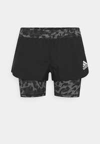 Mustat Adidas-urheilushortsit, joissa on harmaa ja musta kamppailukuosiset sisälegginsit, sekä valkoinen Adidas-logo vasemmalla reisillä.