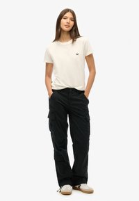 Witte katoenen t-shirt met klein logo, gecombineerd met zwarte cargobroek met zakken en een relaxte pasvorm. Beige sneakers maken de outfit compleet.