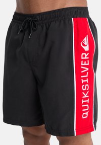 Μαύρα μαγιό σορτς με ρυθμιζόμενο κορδόνι, με έντονη κόκκινη κάθετη ρίγα και λευκές λεπτομέρειες στο πλάι με το κείμενο «QUIKSILVER».